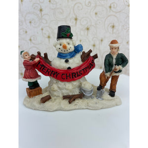 Snowman Figurine - Children Building a Snowman Holding a Merry Christmas Banner